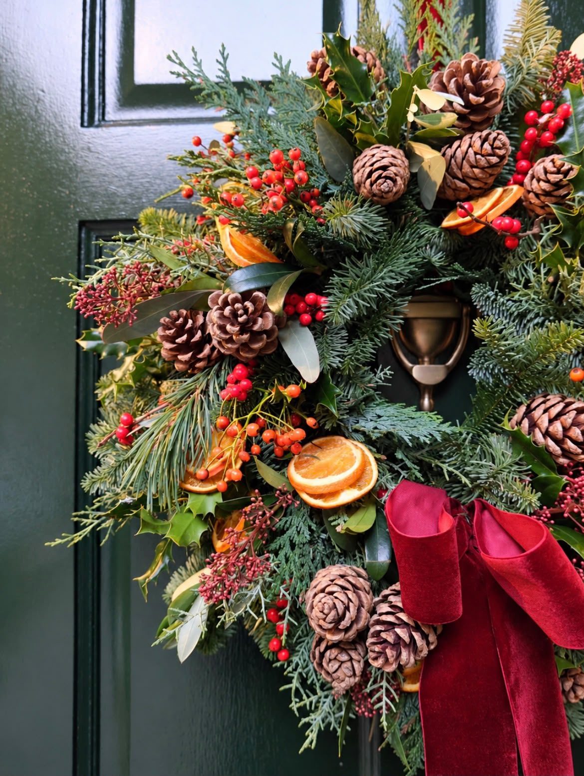 Christmas door wreath with pine cones, orange slices and a red velvet bow
