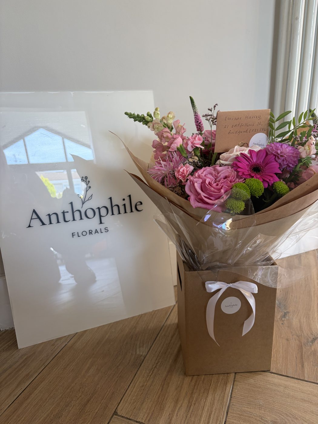 Pink bouquet in a gift bag beside the Anthophile Florals sign