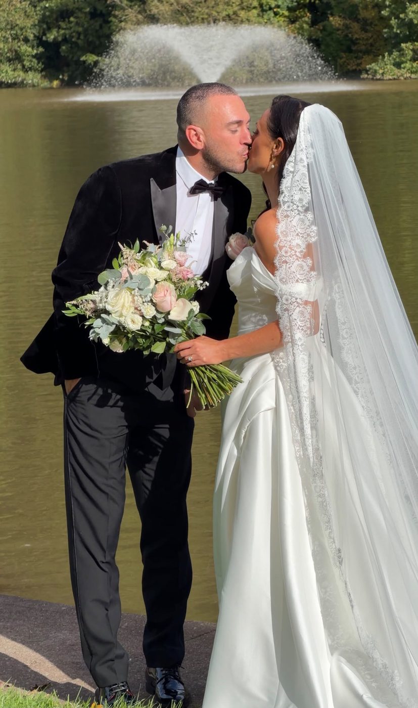 Couple kissing by a lake, bride holding a pastel bouquet